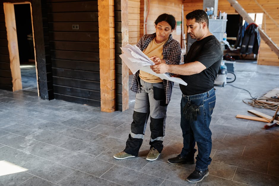 Two workers examining blueprints inside a building under construction, showcasing teamwork.